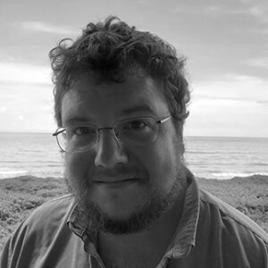 Josh Haven author photo. Black and white headshot of curly-haired man on a beach