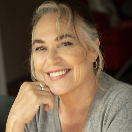 Amy Bloom author photo. Headshot of a woman in a gray shirt with her hand under her chin.